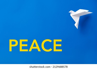 Word Peace in yellow letters on a blue background, colors of the Ukrainian flag, next to a white origami paper dove, symbol of peace. - Shutterstock ID 2129688578