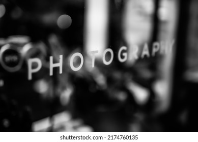 The word "photography" displayed via decal on a storefront glass window in a sans serif font. Black and white monochrome photo. Close up. 