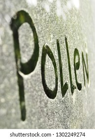 The word pollen spelled on a windshield that is filled with a thick layer of green pollen