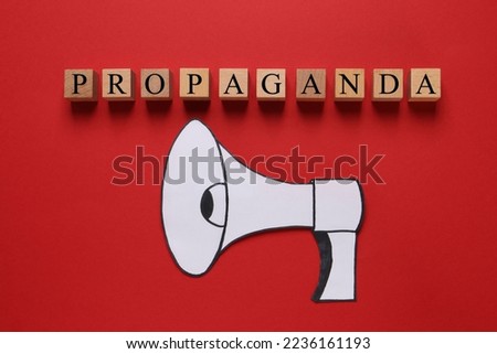Word Propaganda made of wooden cubes and paper loudspeaker on red background, flat lay. Information warfare concept