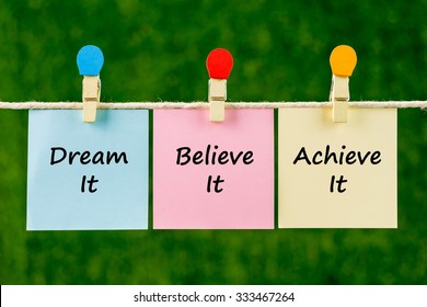 Word Quotes Of Dream It, Believe It, Achieve It On Sticky Color Papers Hanging On Rope Against Blurred Green Background.