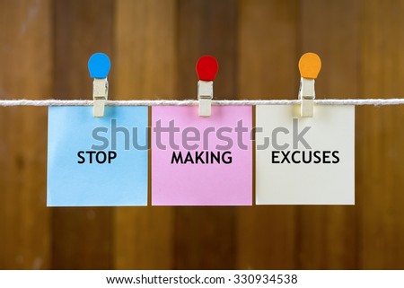 Word quotes of STOP MAKING EXCUSES on colorful sticky papers hanging by a rope against blurred wooden background.