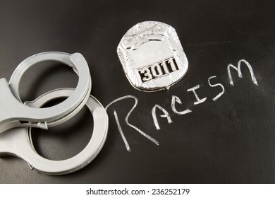 The Word RACISM On A Chalkboard With A Police Badge And Handcuffs