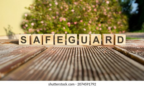 the word safeguard is written on wooden cubes. the blocks are placed on an old wooden board illuminated by the sun. in the background is a brightly blooming shrub