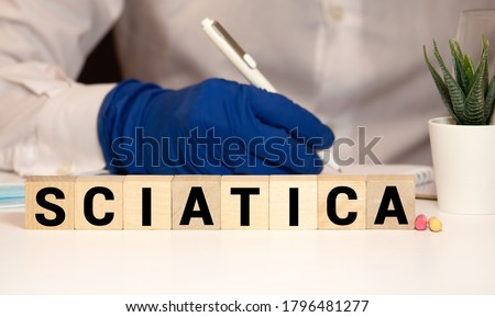 Word sciatica from white blocks and red circle dot on dark fabric background. Orthopedics, neurology pain. leg pain, tingling, numbness, weakness Sciatic Nerve. Medical concept