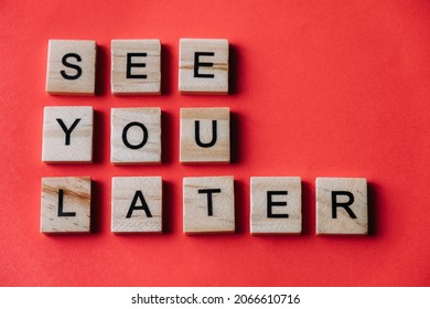 The Word See You Later Is Written In Three Rows Of Wooden Blocks And Letters On A Red Paper Background. Copy Space