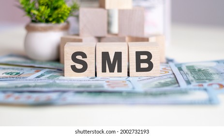 Word SMB Is Written On Wooden Cubes. The Cubes Are Located On The Banknotes Lying On The Table. In The Background A Green Plant In A Pot. SMB - Short For Server Message Block