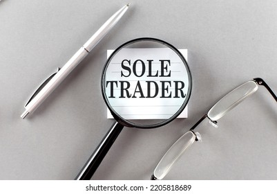 Word SOLE TRADER On A Sticky Through Magnifier On Grey Background