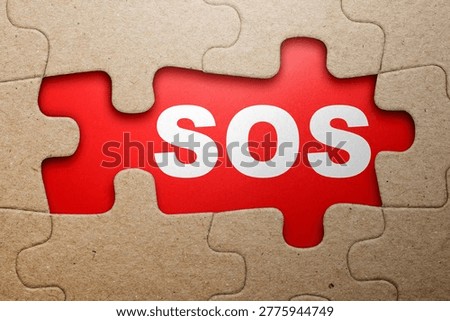 The word SOS is revealed through a missing section of a cardboard jigsaw puzzle, set against a red background to signify a distress call or critical need
