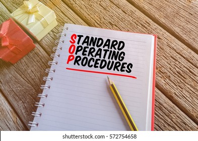 Word STANDARD OPERATING PROCEDURES Written On A Book With Gift Boxes Against Wooden Table. 