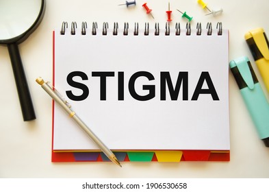 the word stigma is written on a notebook and a white background with a half-glass of colored pencils. High quality photo