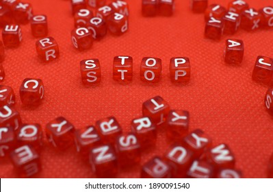 The word stop made of small red cubes with white letters on a red background. There are other letter cubes scattered around - Shutterstock ID 1890091540