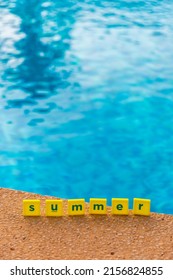 Word Summer Made Of Scrabble Type Letters By The Swimming Pool. Blue Water, Small Yellow Squares With Dark Green Letters. 