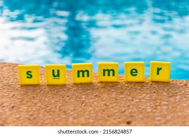 Word Summer Made Of Scrabble Type Letters By The Swimming Pool. Blue Water, Small Yellow Squares With Dark Green Letters. 