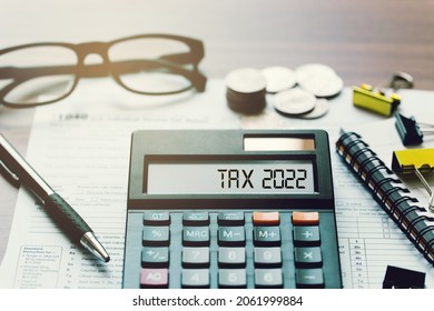 Word Tax 2022 on the calculator. Business and tax concept.Calculator, currency, book, tax form, and pen on wooden table.Top view.