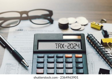 Word Tax 2024 on the calculator. Business and tax concept.Calculator, coins, book, form, and pen on table.Tax deduction planning.Financial research, government taxes, and calculation tax return