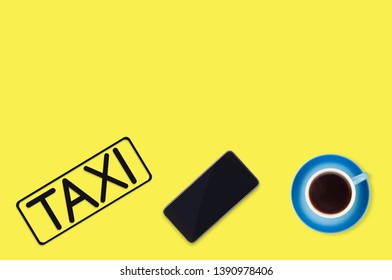 Word Taxi In Frame Of Black Color Cut Out Of Black Paper Near Full Blue Cup Of Coffee And Mobile Phone On Yellow Background. Top View. Taxi Call Concept. Copy Space