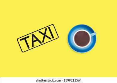 Word Taxi In Frame Of Black Color Cut Out Of Black Paper Near Full Blue Cup Of Hot Chocolate On Yellow Background. Top View. Concept Of Journey. Copy Space