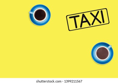 Word Taxi In Frame Of Black Color Cut Out Of Black Paper Near Full Blue Cups Of Hot Chocolate And Coffee On Yellow Background. Top View. Concept Of Journey. Copy Space