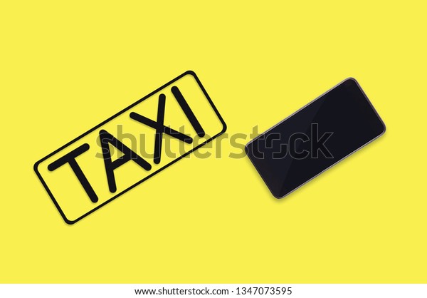 Word taxi in frame of black color cut out of\
black paper near mobile phone on yellow background. Top view. Taxi\
call concept