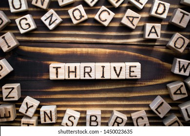 word thrive composed of wooden cubes with letters, to grow, develop, or be successful concept, scattered around the cubes random letters, top view on wooden background
