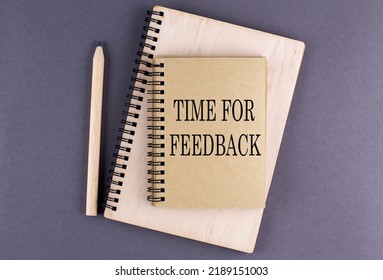 Word TIME TO FEEDBACK on a notebook with pencil on the grey background