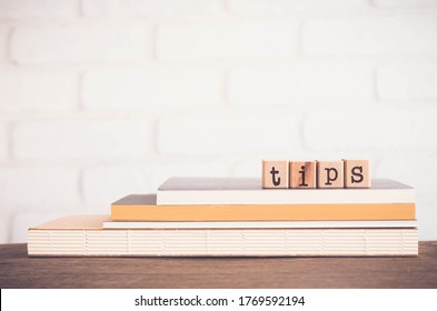 The word TIPS, letters on wooden block cubes on top of books and table with white bricks background,  blank copy space, vintage minimal style. Concepts of  tricks, hack, help, guideline, useful hint.