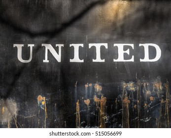 The Word 'UNITED' Painted On Black Painted Steel With Several Patches Of Rust Penetrating Layers Of Time And Neglect. / United /