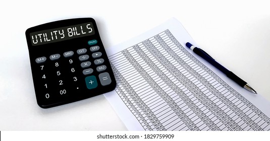The word utility bills on the calculator.A sheet of paper with a table and numbers, a pen on a white background.