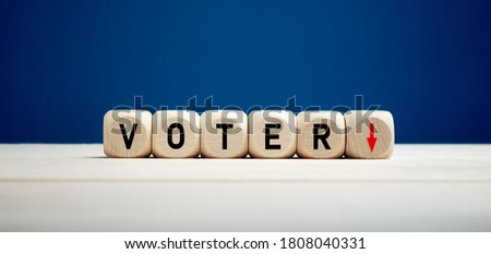 The word voter with downward arrow on wooden cubes. Elections and decreasing voter turnout concept.