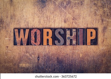 The word "Worship" written in dirty vintage letterpress type on a aged wooden background.
