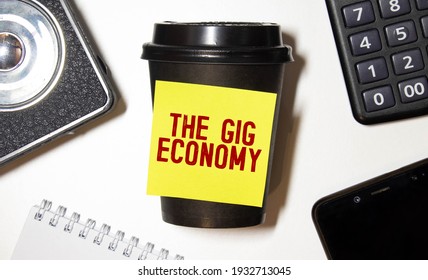 Word Writing Text The Gig Economy. Business Concept For Market Of Short-term Contracts Freelance Work Temporary Black Coffee With Coffee Mug Floating Texts On Gray Black Wooden Desk.