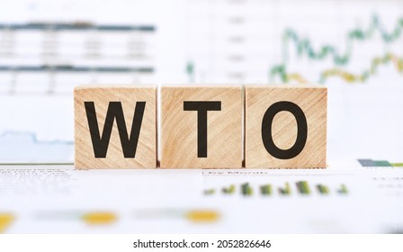 Word WTO - World Trade Organization, Made With Wood Building Blocks On Background From Financial Graphs And Charts.