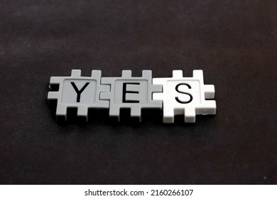 The word YES is composed using a plastic puzzle lying on a table and on a black background.