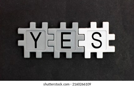 The word YES is composed using a plastic puzzle lying on a table and on a black background.