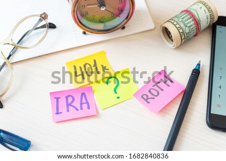 Words 401k ira roth on pieces of colorful paper, money dollars and glasses on table. Pension concept. Retirement plans.