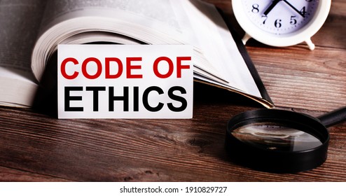 The Words CODE OF ETHICS Written On A White Card Near An Open Book, Alarm Clock And Magnifying Glass