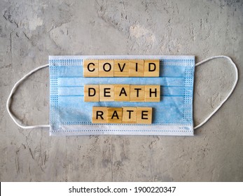 Words COVID DEATH RATE Lined With Wooden Letters On A Background Of Blue Surgical Mask.