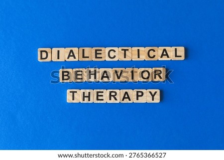 Words: Dialectical Behavior Therapy, spelled out with wooden letter tiles on a blue background. Mental health concept.