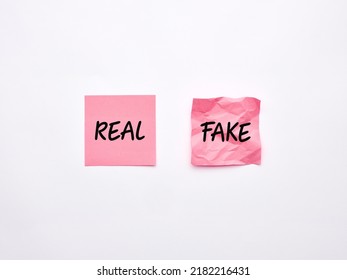 The Words Fake And Real On Pink Sheets Of Note Paper On White Background. Product Imitation Or Genuine Information Concept.