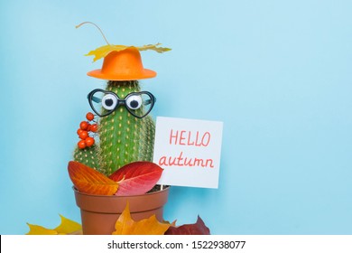 Words Hello autumn, funny cactus and beautiful leaves on the blue background. 
