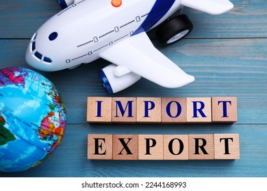 Words Import and Export made of cubes, toy airplane and globe on light blue wooden table, flat lay