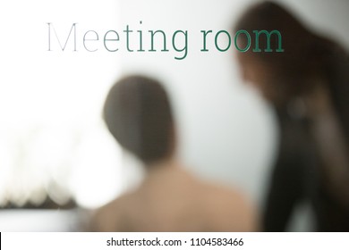Words "Meeting room" written on glass door. Partners talking discussing ideas behind closed office door, business negotiations, meeting room for hour concept. Conference area sign. Close up view.