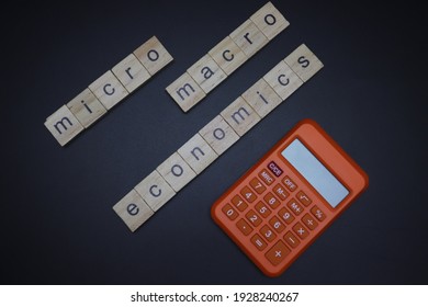 Words Micro And Macro Economics With Calculator Written On Wood Block. Isolated On Dark Background.