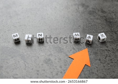 Words Min and Max made of cubes with arrow pointing at it on grey table, closeup