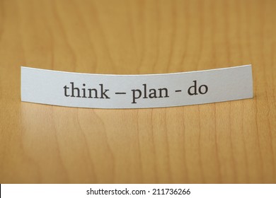 The words Think Plan Do typed on a slip of white paper standing on a wooden pattern background or desktop