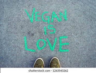 Words Vegan Is Love In Green Chalk Lettering On Cement Sidewalk.