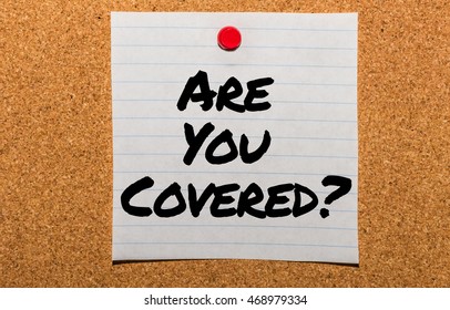 The Words Are You Covered? Typed On A Scrap Of Lined Paper And Pinned To A Cork Notice Board. Asking The Question, Are You Insured For Your Car, Travel, Home Or Other Liability.