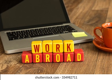 Work Abroad Written On A Wooden Cube In Front Of A Laptop