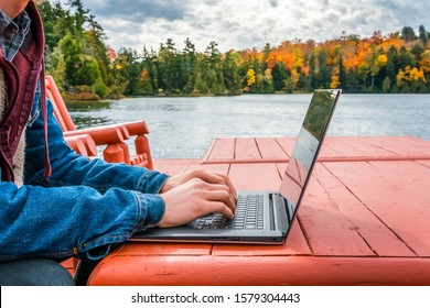 Work from anywhere - working on laptop beneath the autumn sky while on a deck near the water's edge. concept - background